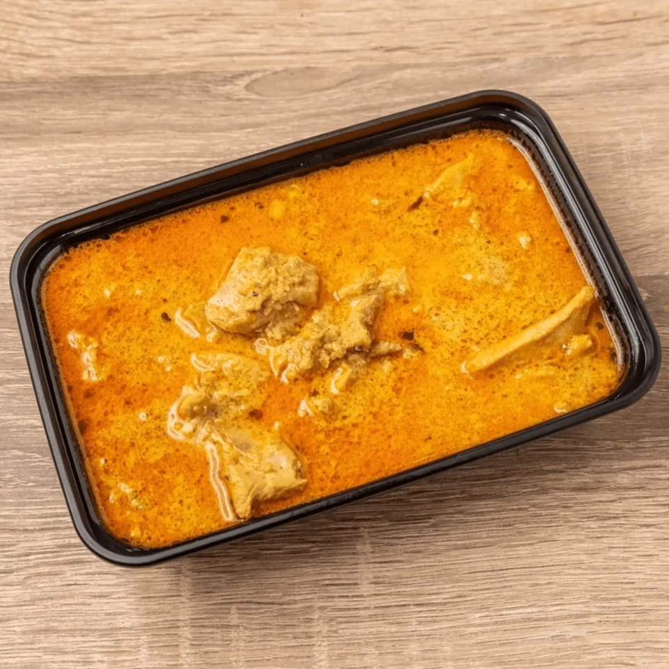 Indian chicken curry in a black rectangular takeout container on a wooden table.