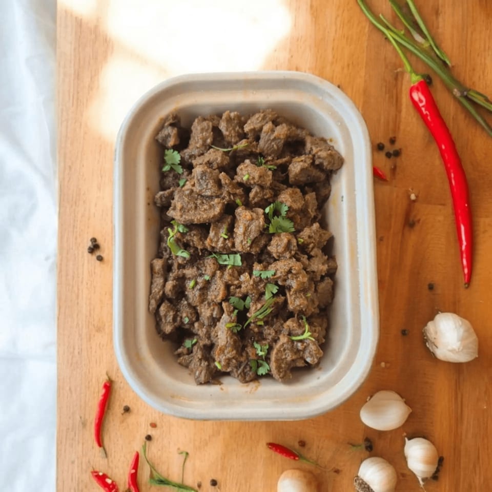 Kolapasi Indian Canteen's beef curry in a takeout container, garnished with cilantro, red chilies, and garlic.