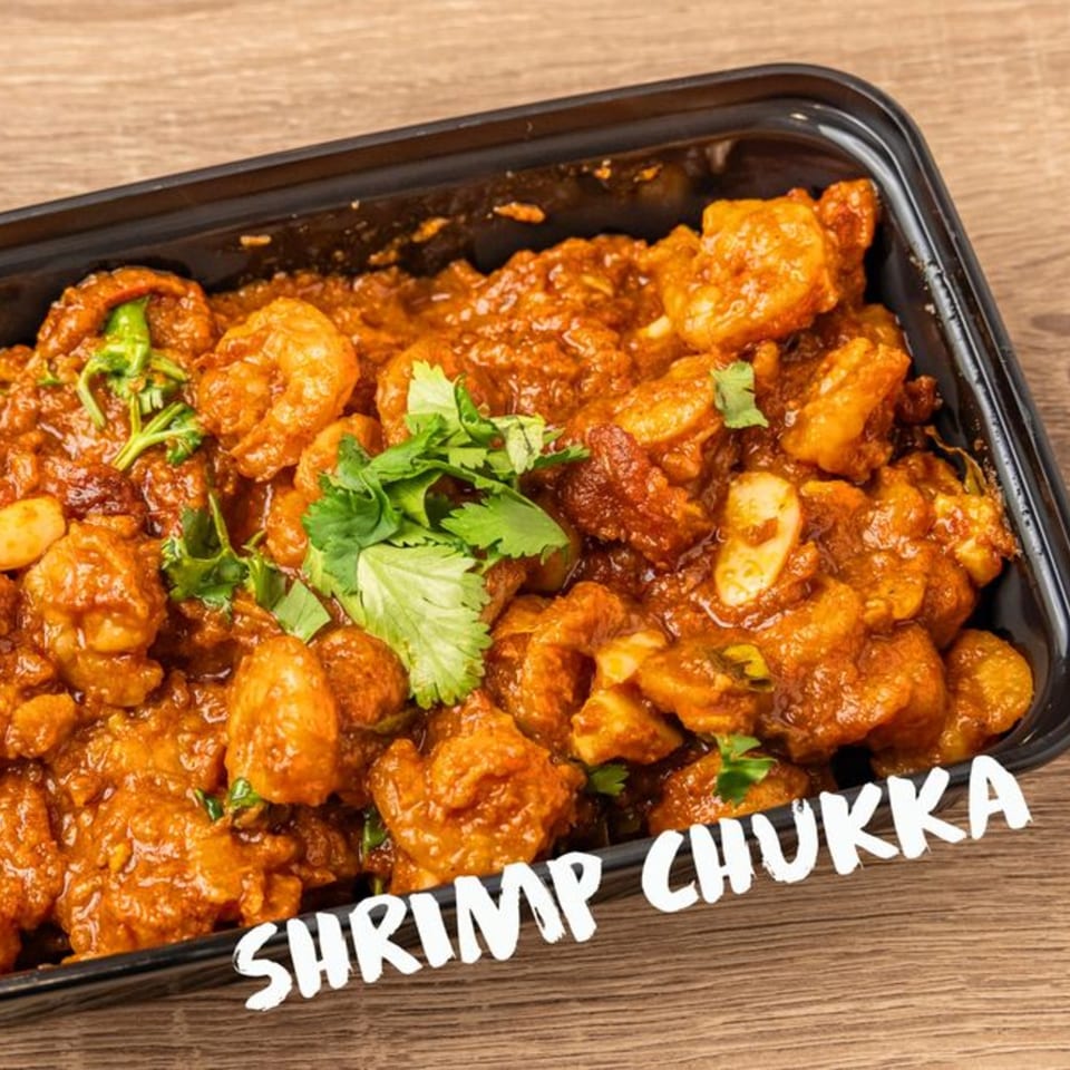 Kolapasi Indian Canteen's Shrimp Chukka, a vibrant orange-red curry with shrimp and cilantro, in a black container.