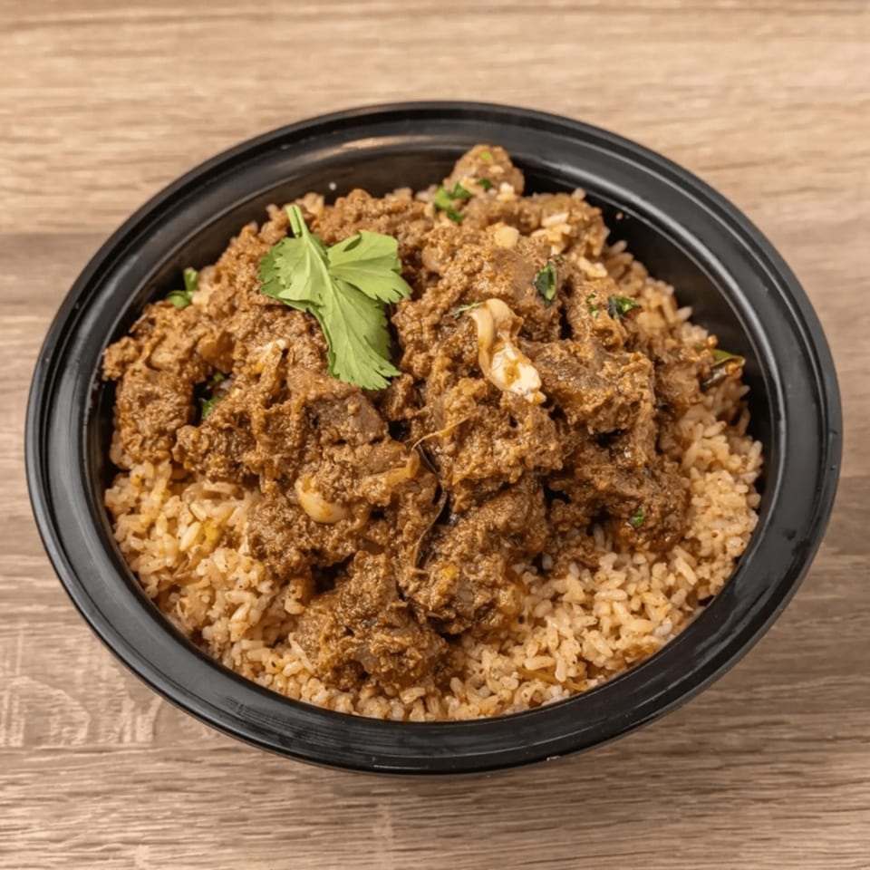 Indian lamb biryani with rice and cilantro in a black bowl on a wooden table.